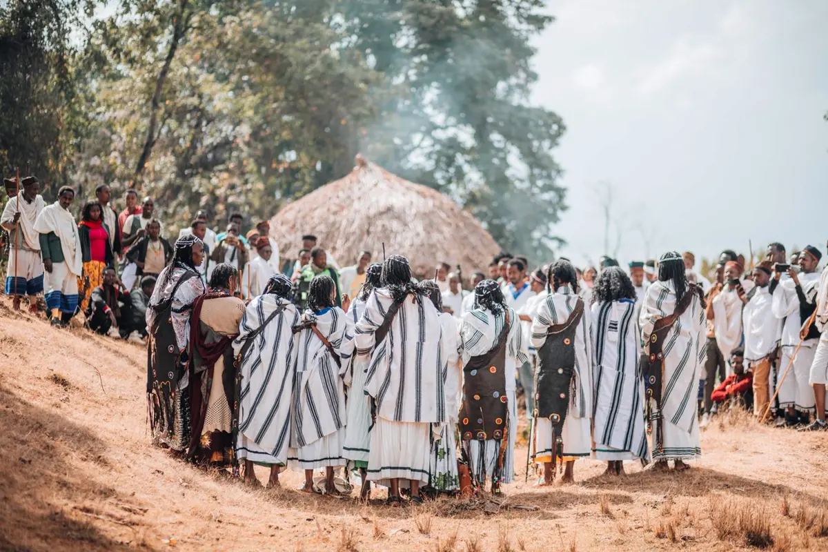 A wide circle of people in striped cloth gathered around a compound.
